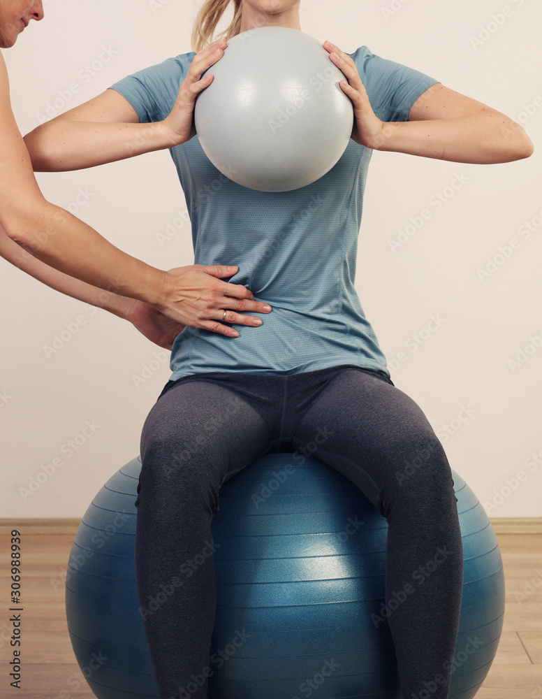 Trainer guiding client through corrective exercise on stability ball